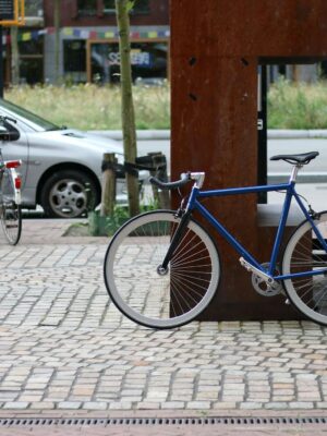 A blue fixie bike parked on a cobblestone street in an urban setting, showcasing city life.