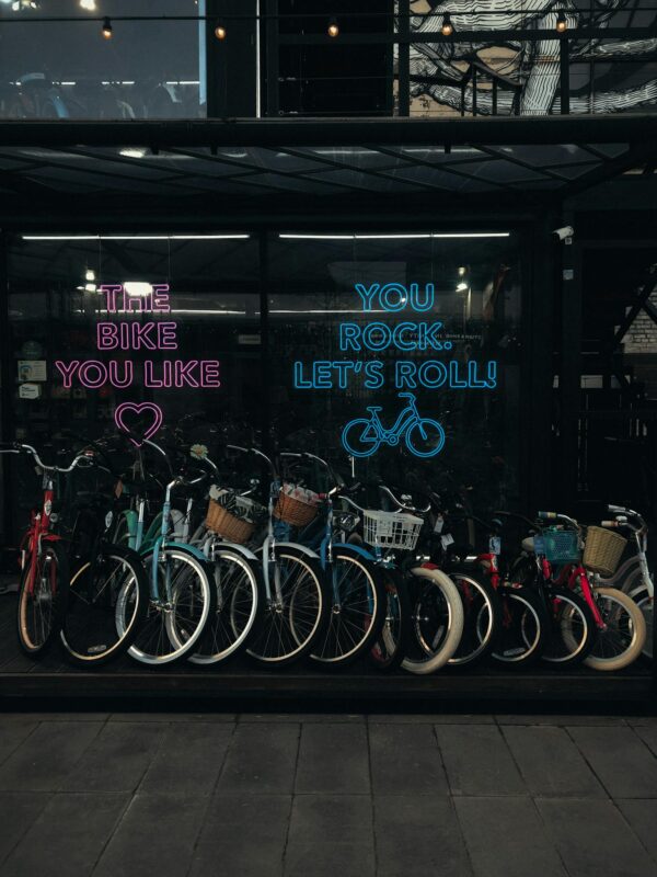 A vibrant row of bicycles for sale in an urban bike shop with neon signs at dusk.