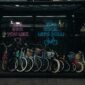 A vibrant row of bicycles for sale in an urban bike shop with neon signs at dusk.