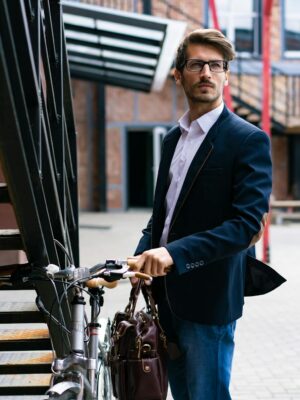 Elegant businessman with bicycle in cityscape, wearing a suit and carrying a briefcase.