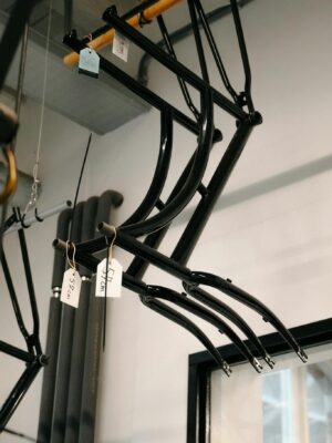 Hanging black steel bicycle frames in an Amsterdam workshop with natural lighting.